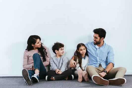 Family of four sitting o floor against wall