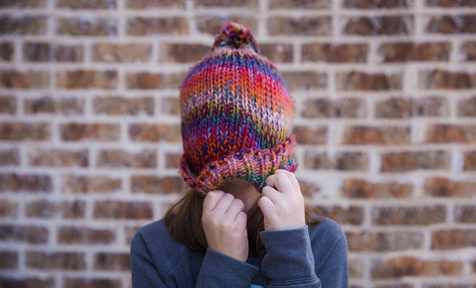 Girl with colorful wool cap pulled over face against brick wall