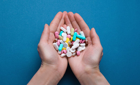 Hands holding many pills against blue background
