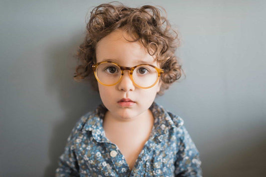 Young boy with curly hair and glasses making a straight face.