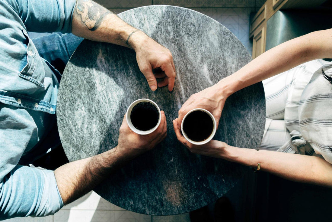 Two people sitting at a table holding coffee cups.