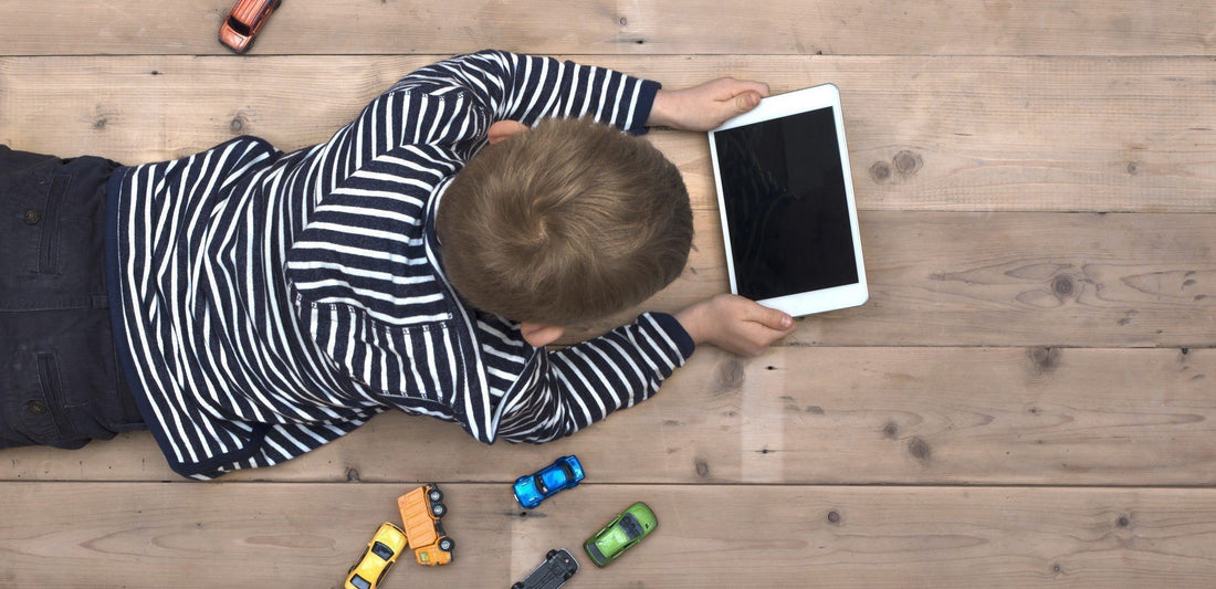 Young boy lying on floor with toys and tablet