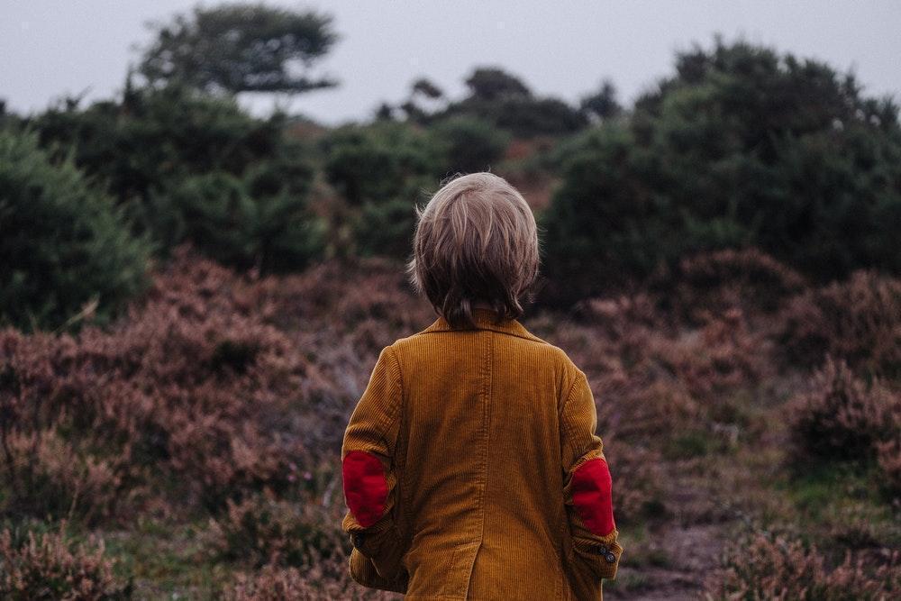 child outdoors looking at a hill covered with shrubs