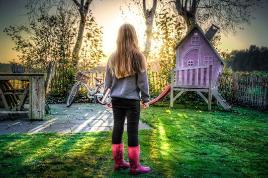 Young girl in yard with playhouse and bicycle.
